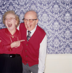 Senior couple standing together laughing, indoors, portrait