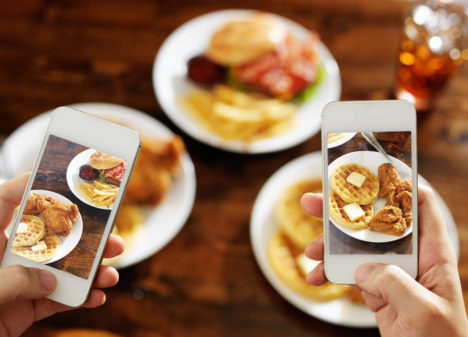 two friends taking photo of their food with smartphones over ar restaurant table