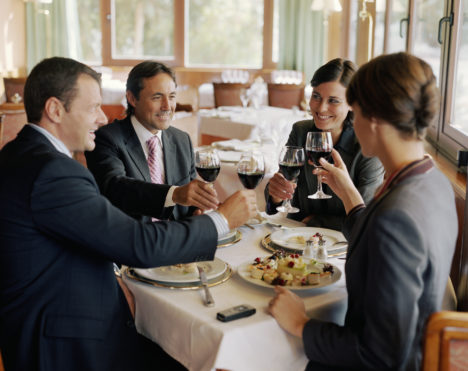 Two businessmen and women at restaurant table, raising glasses